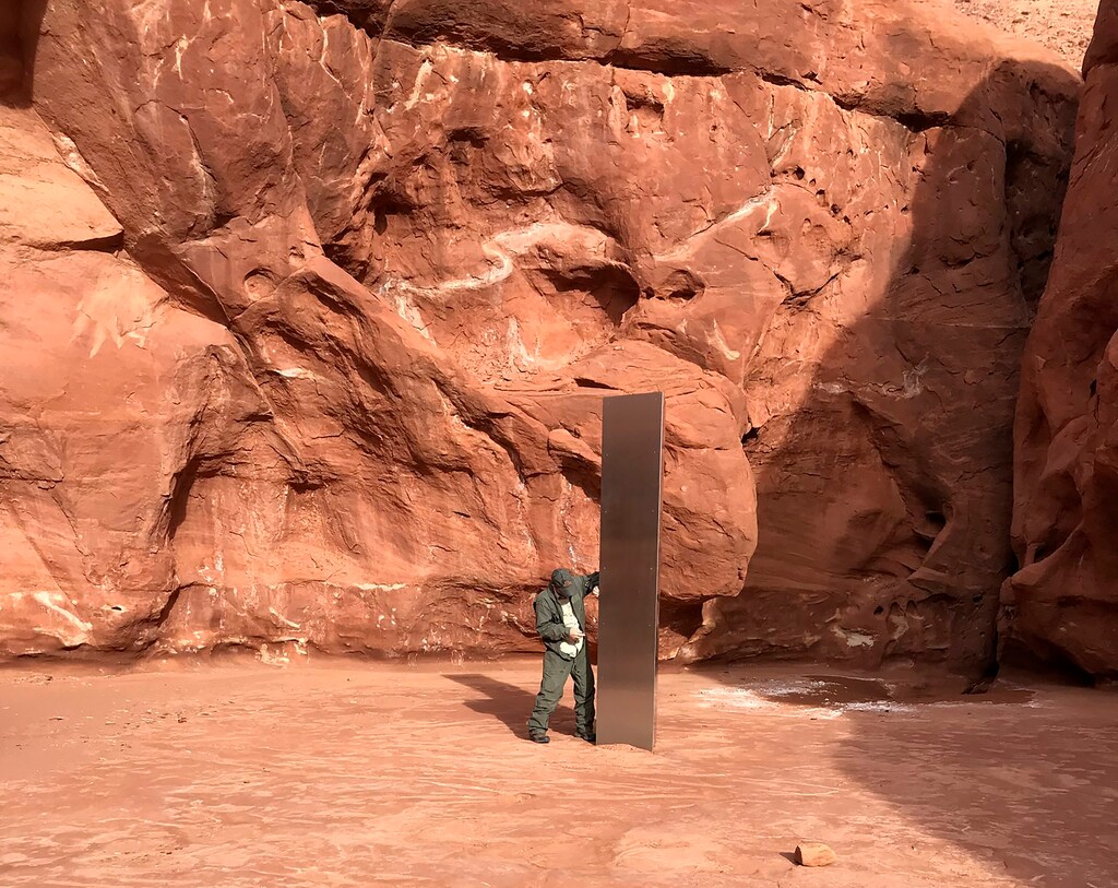 (Utah Department of Public Safety via AP) A Utah state worker stands next to a metal monolith in the ground in a remote area of red rock in Utah on Nov. 18, 2020.