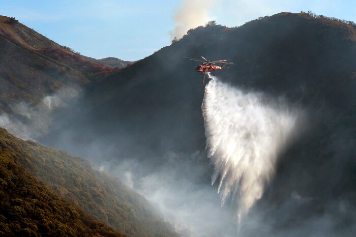(Mike Eliason | Santa Barbara County Fire Department via AP) In this photo provided by the Santa Barbara County Fire Department, a Sikorsky S-64 Skycrane makes a water drop on hot spots along the hillside east of Gibraltar Road in Santa Barbara, Calif., Sunday morning, Dec. 17, 2017. One of the largest wildfires in California history is now 40 percent contained but flames still threaten coastal communities as dry, gusty winds are predicted to continue.