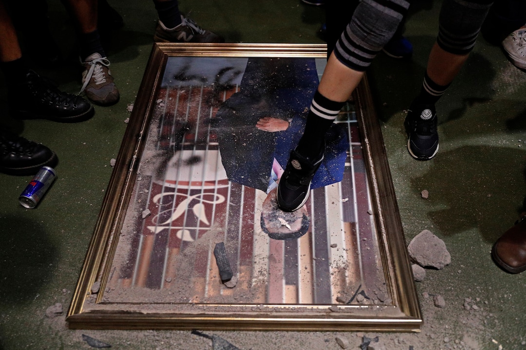 (Vincent Yu | AP Photo) A protester steps on a damaged portrait of former legislative leader lie on the ground after protesters broke into the Legislative Council building in Hong Kong, Monday, July 1, 2019. Protesters in Hong Kong took over the legislature's main building Monday night, tearing down portraits of legislative leaders and spray painting pro-democracy slogans on the walls of the main chamber.