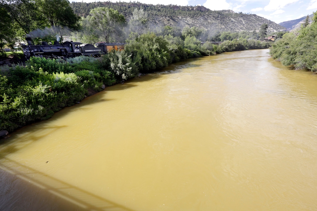 The Animas River is still flowing with toxic waste from the Gold King Mine on Saturday, Aug. 8, 2015, as seen from the 32nd Street Bridge in Durango, Colo., as the Durango & Silverton Narrow Gauge Railroad train goes by. (Jerry McBride/The Durango Herald via AP)