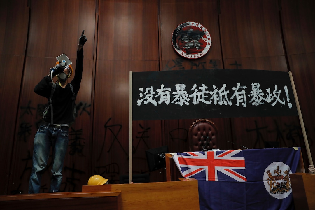 (Kin Cheung | AP Photo) A protester shouts next to a defaced Hong Kong emblem and a banner reads "No thug, only tyranny" after they broke into the Legislative Council building in Hong Kong, Monday, July 1, 2019. Protesters in Hong Kong took over the legislature's main building Monday night, tearing down portraits of legislative leaders and spray painting pro-democracy slogans on the walls of the main chamber.