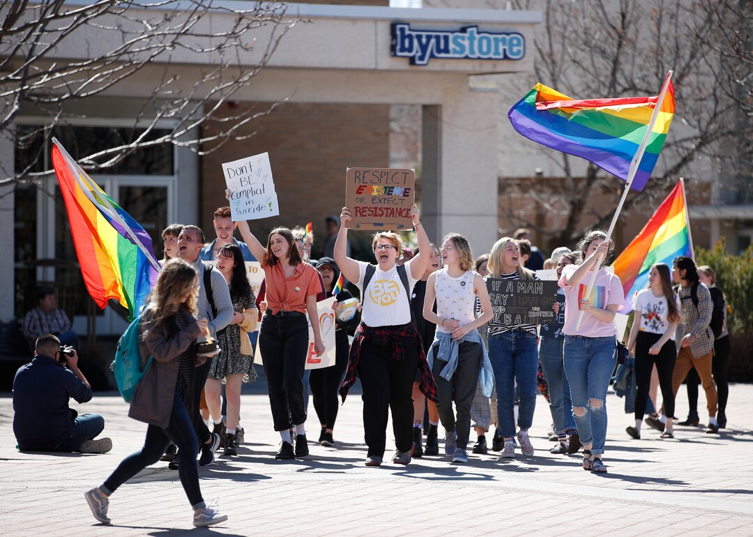 (George Frey  |  special to The Salt Lake Tribune) A BYU student walks by other BYU students in front of the Ernest L. Wilkinson Student Center on the campus of Brigham Young University protesting BYUÕs rollback of a newly announced policy change on LGBTQ students on March 5, 2020 in Provo, Utah.