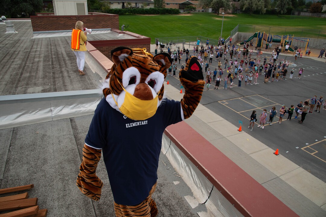 (Francisco Kjolseth  |  The Salt Lake Tribune)  Home of the Cubs, Canyon View Elementary school mascot Bennie, played by PTA president Emily Weigel waves to kids as school principal Kierstin Draper uses a megaphone to greet students back from the roof of the school. It was the first day of classes for the Canyons School District on Monday, August 24, 2020.