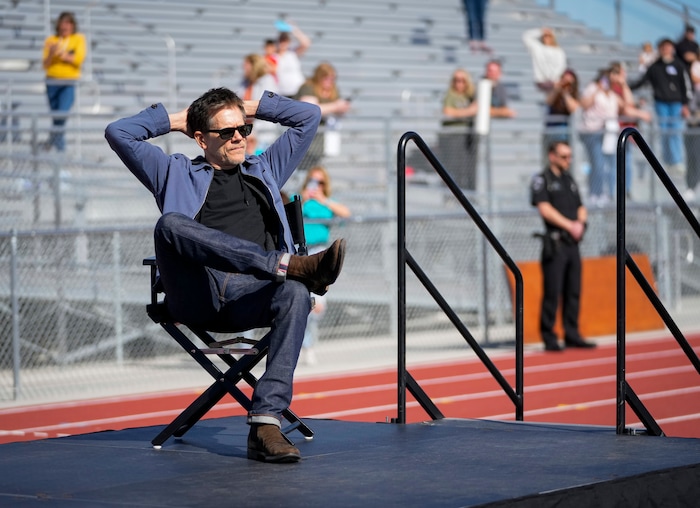 (Bethany Baker | The Salt Lake Tribune) Keivn Bacon sits in a director's chair for him on stage at a charity event to commemorate the 40th anniversary of the movie "Footloose" on the football field of Payson High School in Payson on Saturday, April 20, 2024.