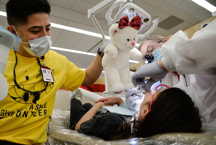 (Francisco Kjolseth  |  The Salt Lake Tribune) Daniel Chavez, left, a second-year dental student at the University of Utah helps distract a young patient getting an extraction by Dr. Tom Liddell on Saturday, Feb. 29, 2020 as part of the American Dental Association’s “Give Kids a Smile” program. The effort launched in 2003 gives no-cost care to thousands of kids nationwide.