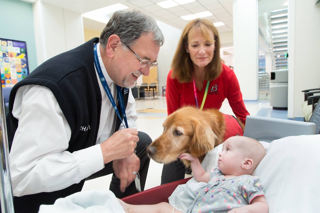 (Photo courtesy Schwarz Center for Compassionate Healthcare) Chaplain David Pascoe, joined here by a comfort dog, visits one of hundreds of young patients at Primary Children's Hospital.