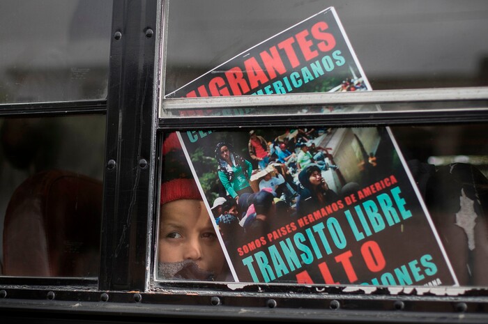 A Central American child who is traveling with a caravan of migrants, peers from a bus carrying the group to the border wall for a gathering of migrants living on both sides of the border, in Tijuana, Mexico, Sunday, April 29, 2018. The sign reads in Spanish: We're all brother countries from the Americas. Free transit. Stop the deportations." (AP Photo/Hans-Maximo Musielik)