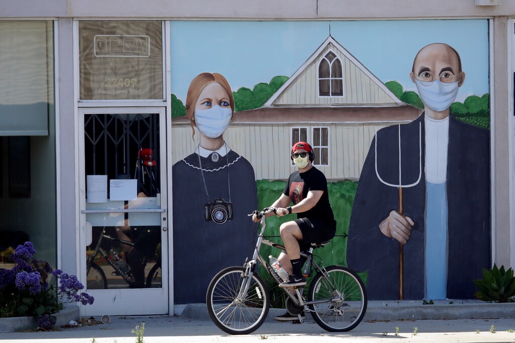 (Marcio Jose Sanchez | AP photo)
In this April 30, 2020, photo, a person wearing a mask cycles past a recently painted mural with a depiction of artist Grant Wood's famed "American Gothic" painting, but with the subjects wearing masks, in Torrance, Calif.