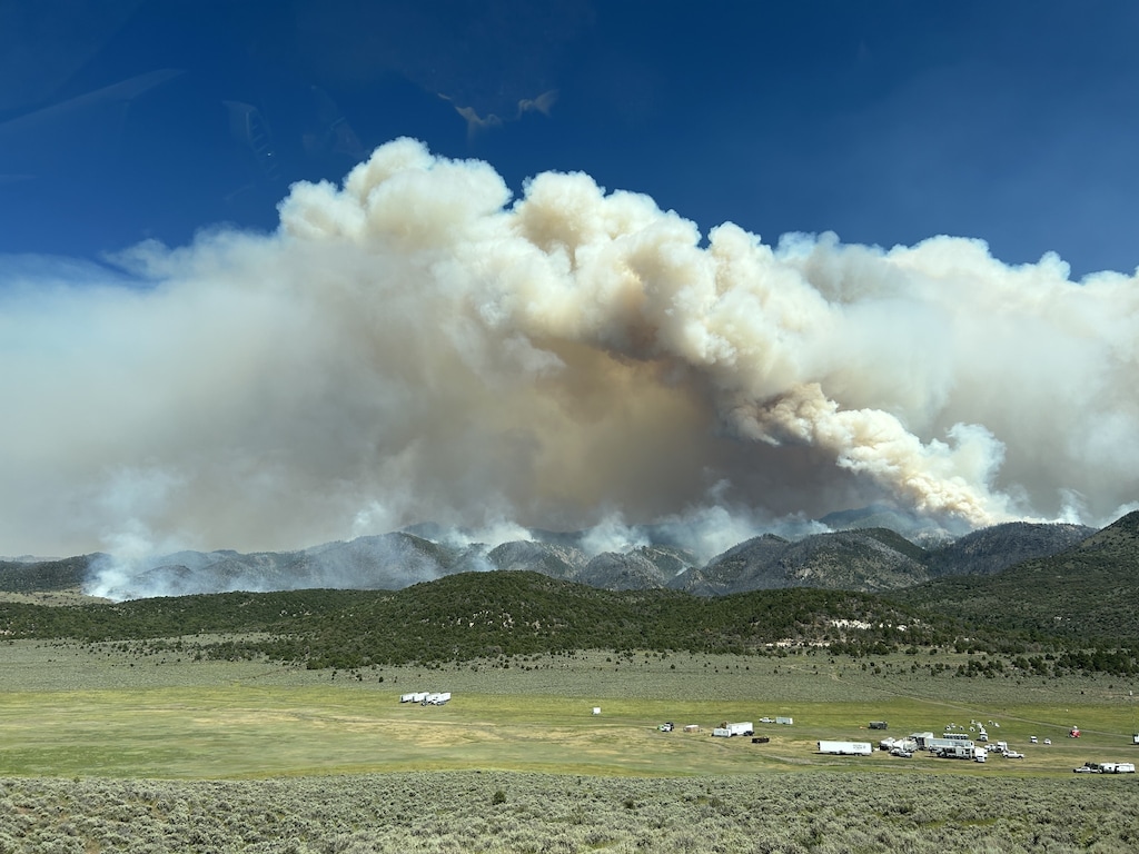 Smoke billows between a green landscape and a dark blue sky.