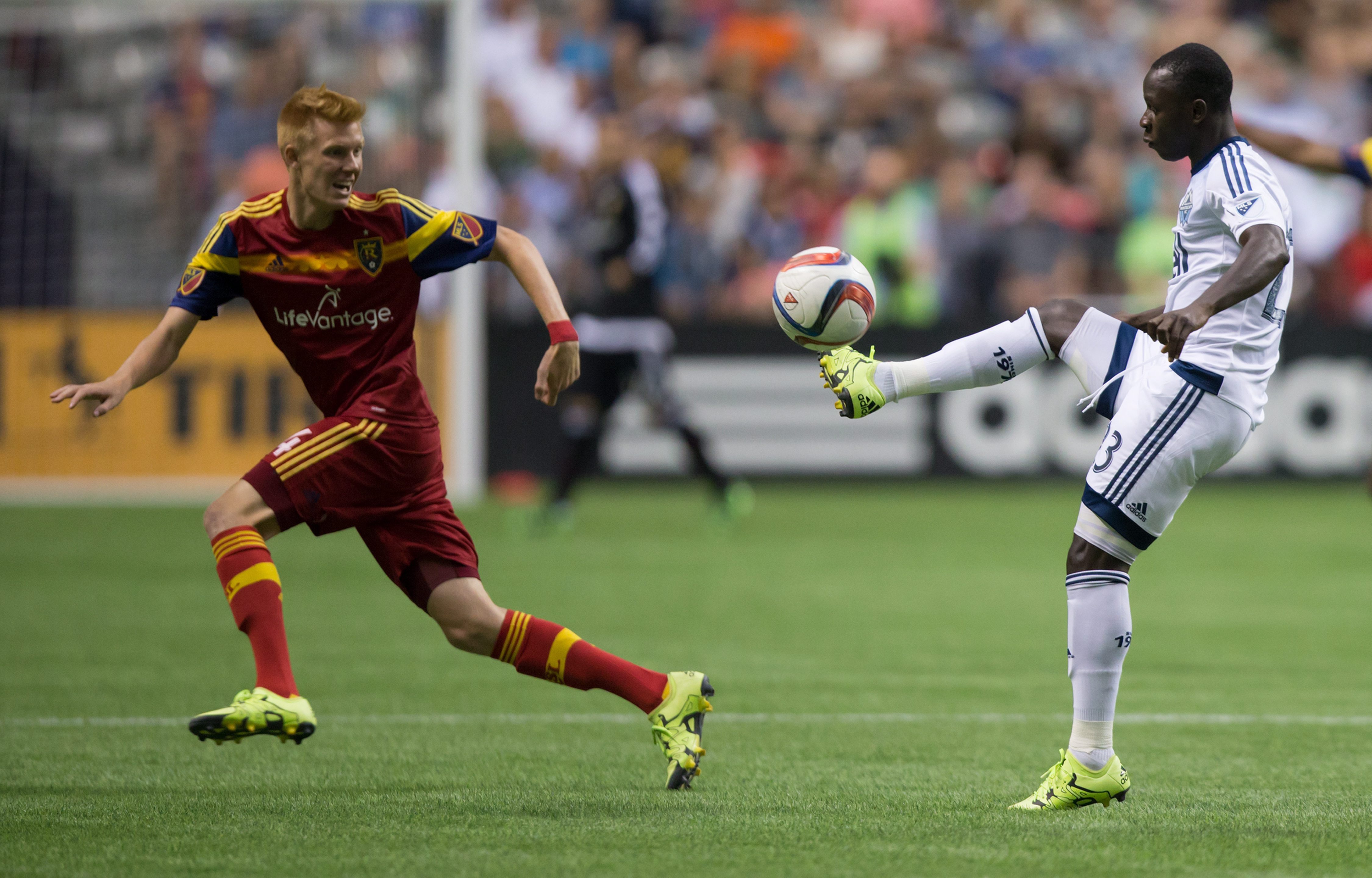 Vancouver Whitecaps' Kekuta Manneh, right, of Gambia, passes the ball over Real Salt Lake's Justen Glad during the first half of an MLS soccer game in Vancouver, British Columbia, Saturday, Aug. 8, 2015. (Darryl Dyck/The Canadian Press via AP) MANDATORY CREDIT