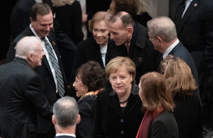 German Chancellor Angela Merkel mingles before the start of State Funeral for former President George H.W. Bush at the National Cathedral, Wednesday, Dec. 5, 2018, in Washington. In the background are former President Jimmy Carter and his wife Rosalynn Carter. (AP Photo/Carolyn Kaster)