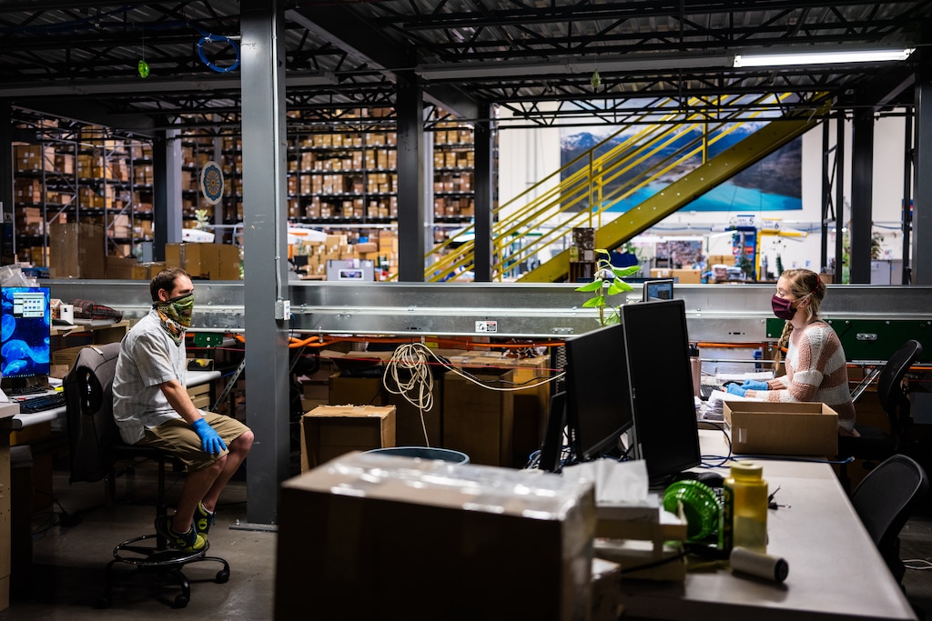 (Max Whittaker | The New York Times) Workers maintain their distance while chatting in the returns department at Patagonia’s distribution center in Reno, Nev., which resumed limited operations last month, on April 24, 2020. Patagonia, one of the first retailers to temporarily close as the coronavirus spread, has lost half its sales in North America and is looking at a transformed landscape.