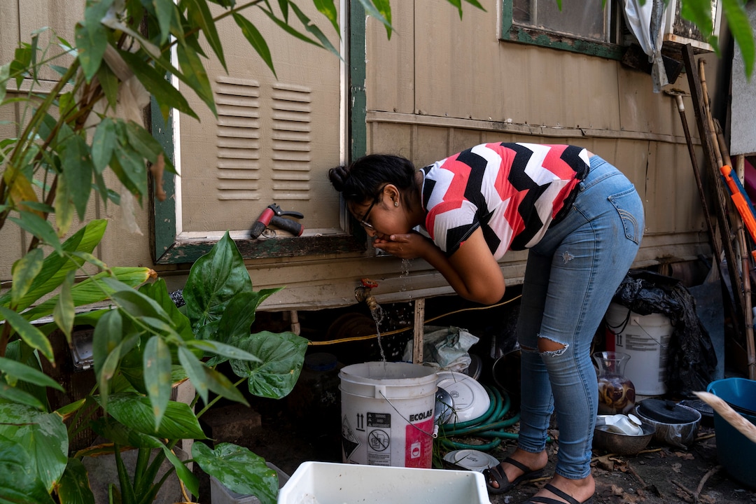 (Ilana Panich-Linsman | The New York Times) Norma Rodriguez, who works two jobs and is planning for community college, cools off with a spigot on the side of her family's trailer in Houston, July 19, 2020. Houston, one of America's fastest-warming cities, could average 109 days a year with the heat index topping 100 degrees.