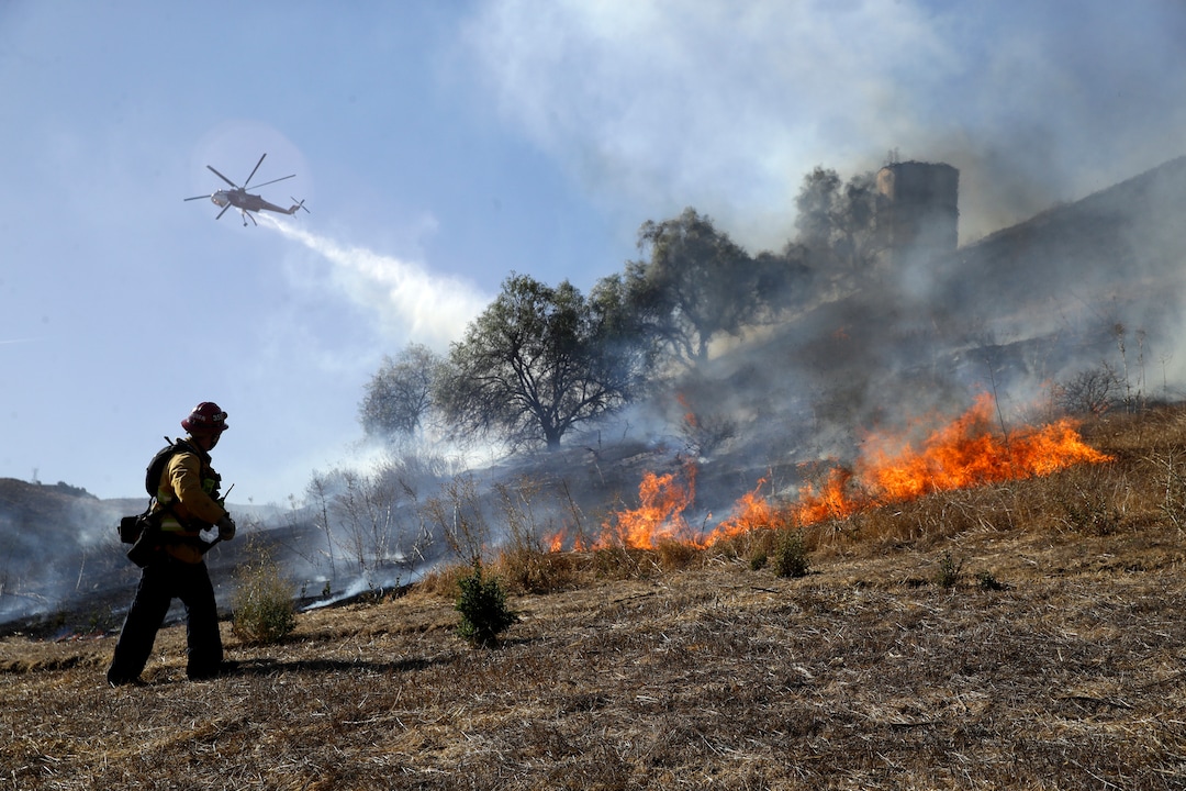 (Marcio Jose Sanchez | AP)  Trinh Nguyen, of the Camarillo Fire Dept, monitors the advance of the Easy Fire as a helicopter makes a water drop Wednesday, Oct. 30, 2019, in Simi Valley, Calif. Driven by powerful Santa Ana winds, the brush fire broke out before dawn between the cities of Simi Valley and Moorpark north of Los Angeles and exploded to more than 1,300 acres (526 hectares), threatening 6,500 homes, Ventura County officials said.