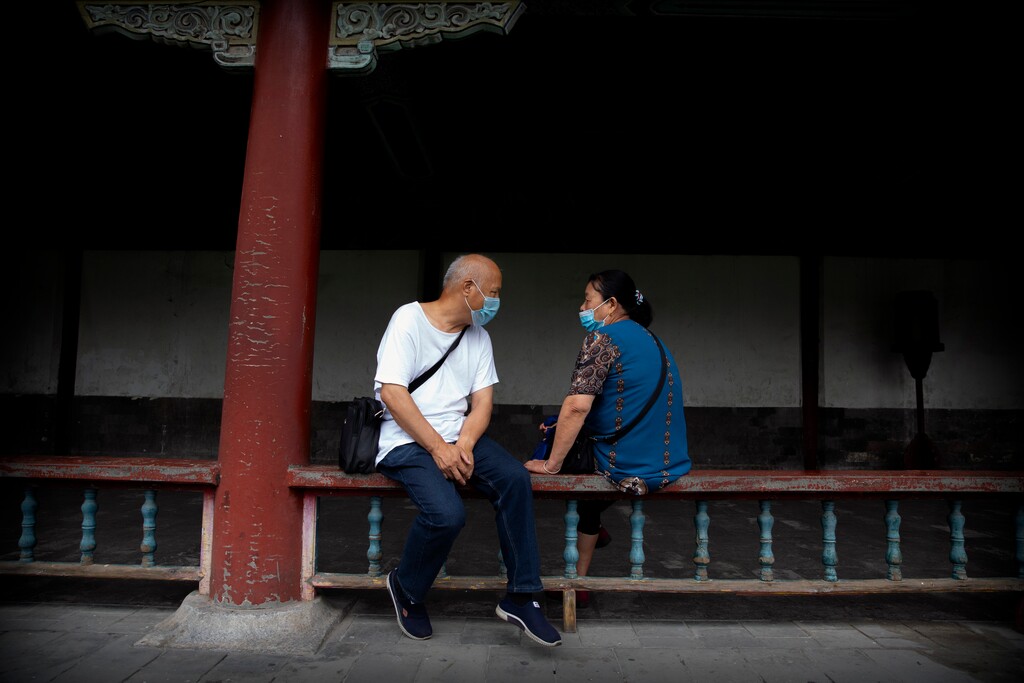 People wearing face masks to protect against the coronavirus sit on a railing at the Temple of Heaven in Beijing, Saturday, July 18, 2020. Authorities in a city in far western China have reduced subways, buses and taxis and closed off some residential communities amid a new coronavirus outbreak, according to Chinese media reports. They also placed restrictions on people leaving the city, including a suspension of subway service to the airport. (AP Photo/Mark Schiefelbein)