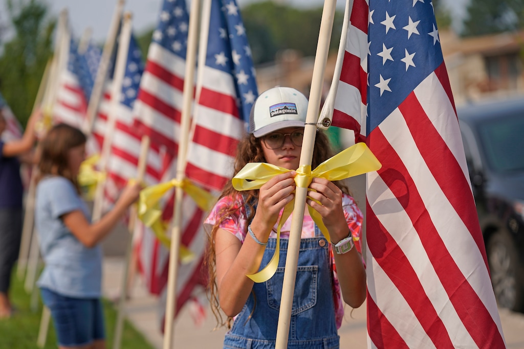 (Rick Bowmer | AP) Neighbors tie yellow ribbons to flags in front of the family home of U.S. Marines Staff Sgt. Taylor Hoover Friday, Aug. 27, 2021, in Sandy, Utah. Hoover was among the 13 U.S. troops killed in a horrific suicide bombing at Afghanistan's Kabul airport, which also claimed the lives of more than 100 Afghans. Hoover had been in the Marines for 11 years, his father Darin Hoover said Friday.