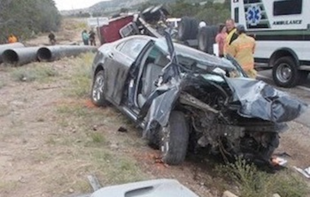 (Utah Highway Patrol) This car was smashed when the semitruck in the background rolled and the pipes it was carrying hit the car.