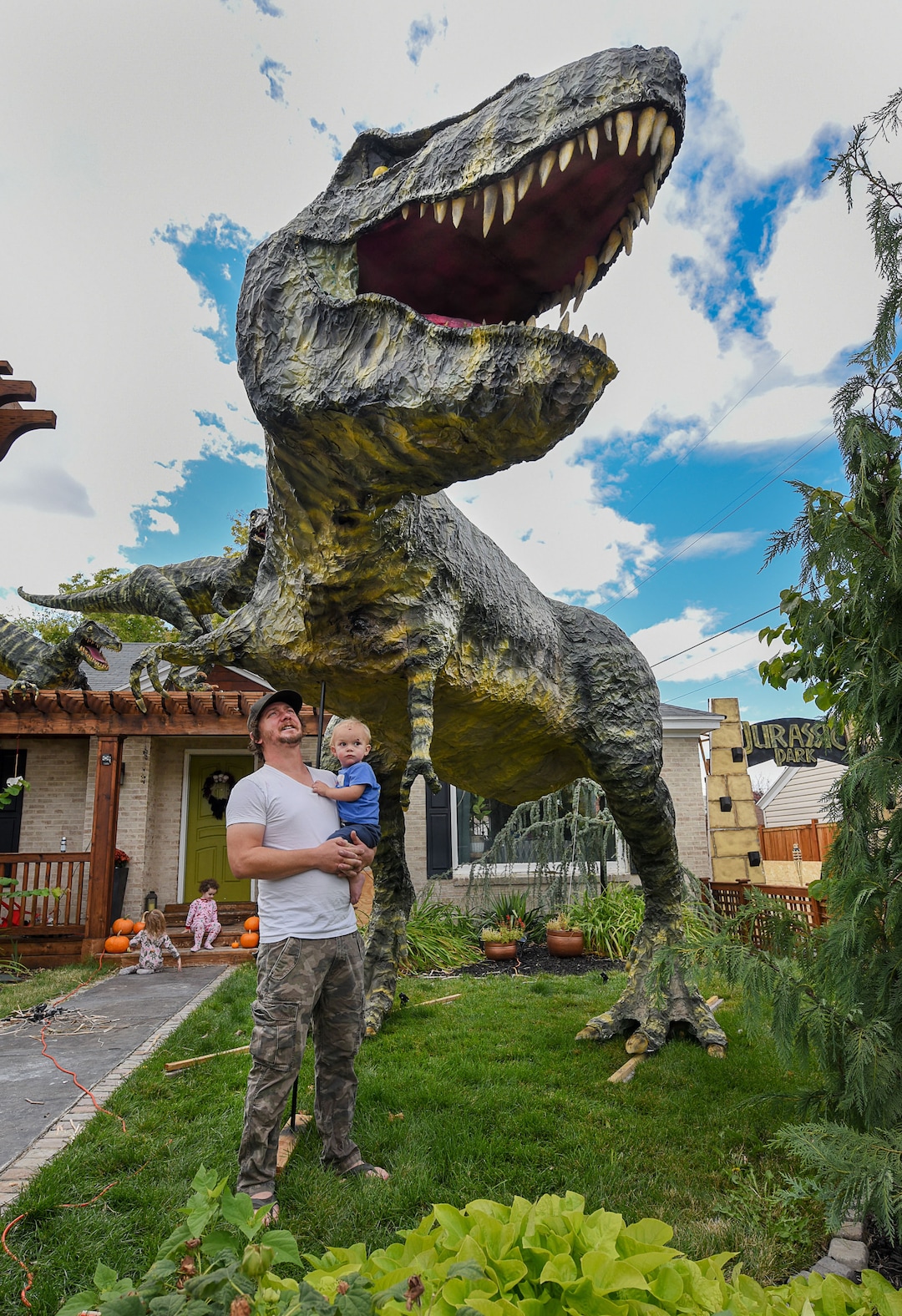 (Francisco Kjolseth  |  The Salt Lake Tribune)  Ammon Smith, holding his nephew Lincoln Smith, 1, has outdone himself once again by going big on his front lawn at 1542 S. 900 East in Salt Lake City for Halloween after constructing a "maturing adult"-size T. rex along with a pair of velociraptors and pterodactyls. The part-time stay-at-home dad, who made a giant King Kong last year, started construction back in August as he assembled recycled wood, chicken wire, foam, aluminum foil and spray paint for the 12-by-32-foot Jurassic centerpiece and companion pieces.
