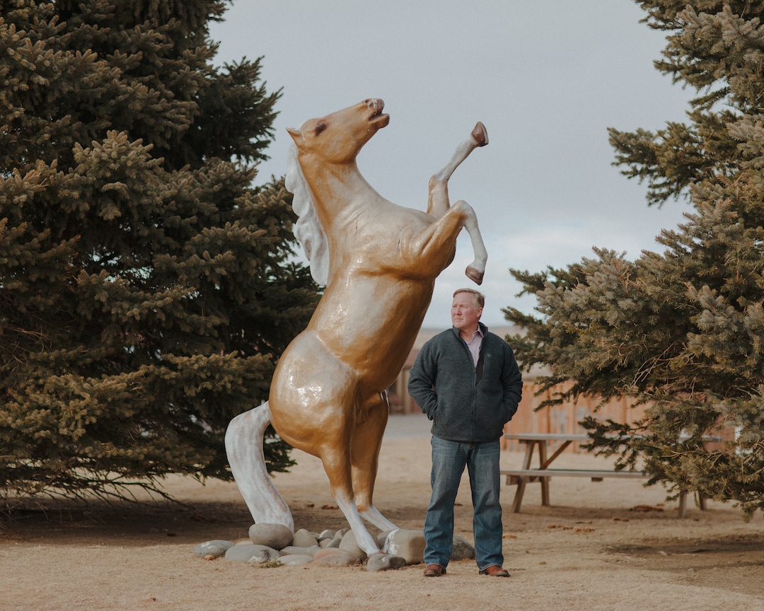 (Elliot Ross | The New York Times) Matt Hall, the mayor of Cody, Wyo., stands with a statue of a horse at the Big Bear Motel in Cody, Jan. 28, 2020. Cody is near Yellowstone National Park, and so its biggest industry is tourism; on summer weekends, its population can grow by about 50 percent, with visitors stopping in to see the rodeo and the nightly recreations of Old West gunfights before heading west to the park.