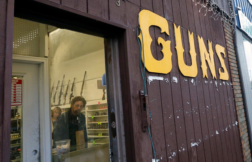(AP Photo/Elaine Thompson,File) This Dec. 19, 2012 file photo show rifles line a wall above in front of people standing in a gun shop in Seattle.
