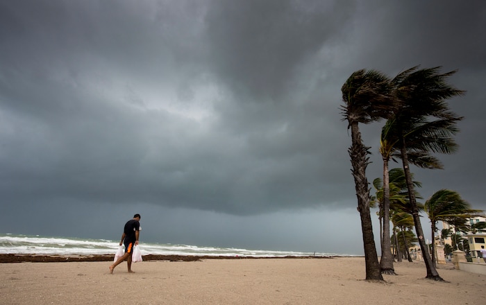 (Paul Chiasson/The Canadian Press via AP) A man walks along the beach with heavy winds and threatening skies in Hollywood, Fla., as Hurricane Irma approaches the state on Saturday, Sept. 9, 2017.