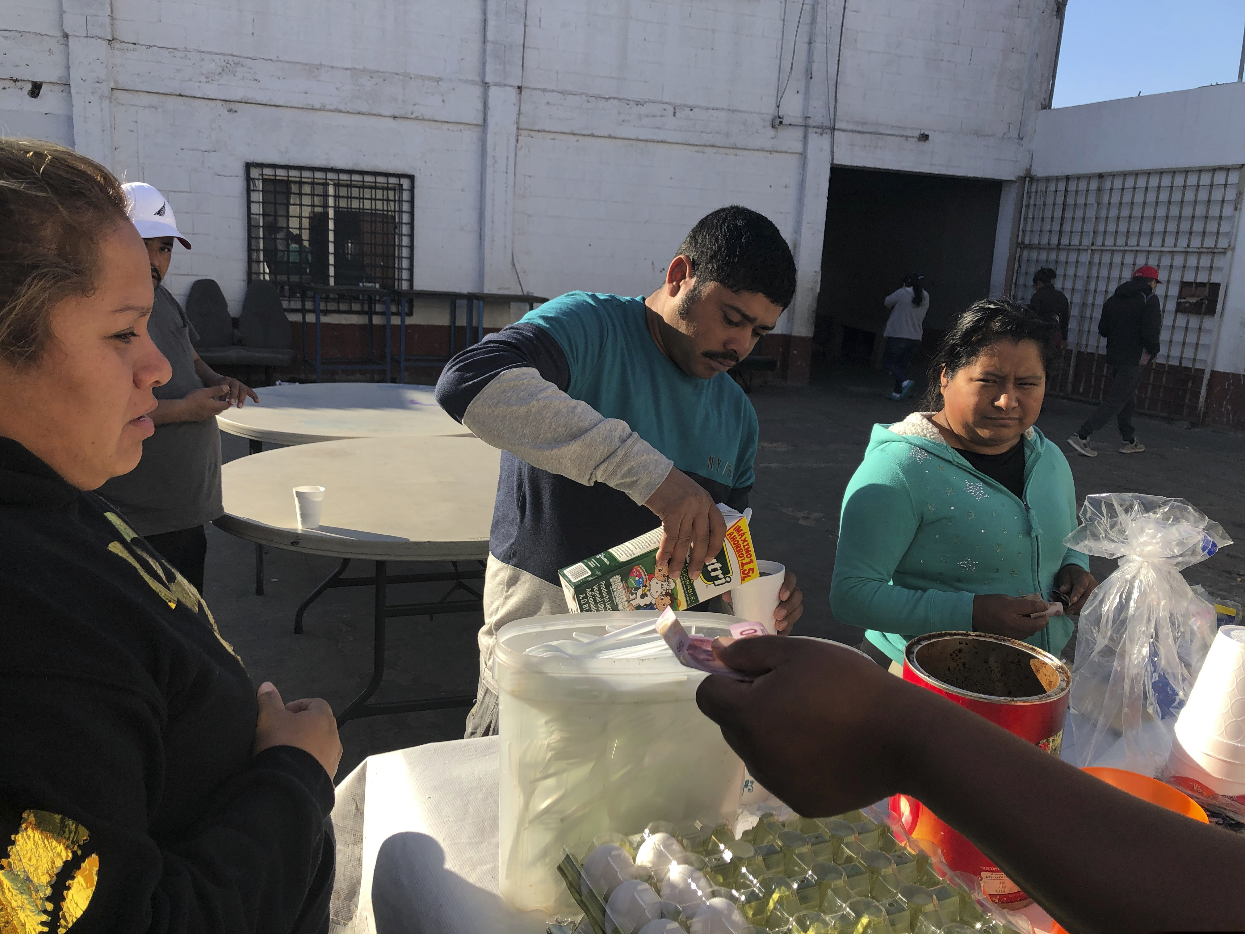 (Elliot Spagat | AP) Joel Caceres, center, pours milk in his coffee as other asylum seekers at a migrant shelter purchase food in Mexicali, Mexico, on Jan. 11, 2010. Caceres, from Honduras, is seeking asylum in San Diego with his wife and two sons. Illegal border crossings have plummeted as the Trump administration has extended a policy to make asylum seekers wait in Mexico for court hearings in the U.S.