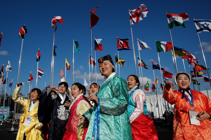 A group of volunteers wearing handbook, Korean traditional dress, greet athletes entering the Olympic Village as flags including North Korea's, fly prior to the 2018 Winter Olympics in Gangneung, South Korea, Thursday, Feb. 1, 2018. (AP Photo/Jae C. Hong)