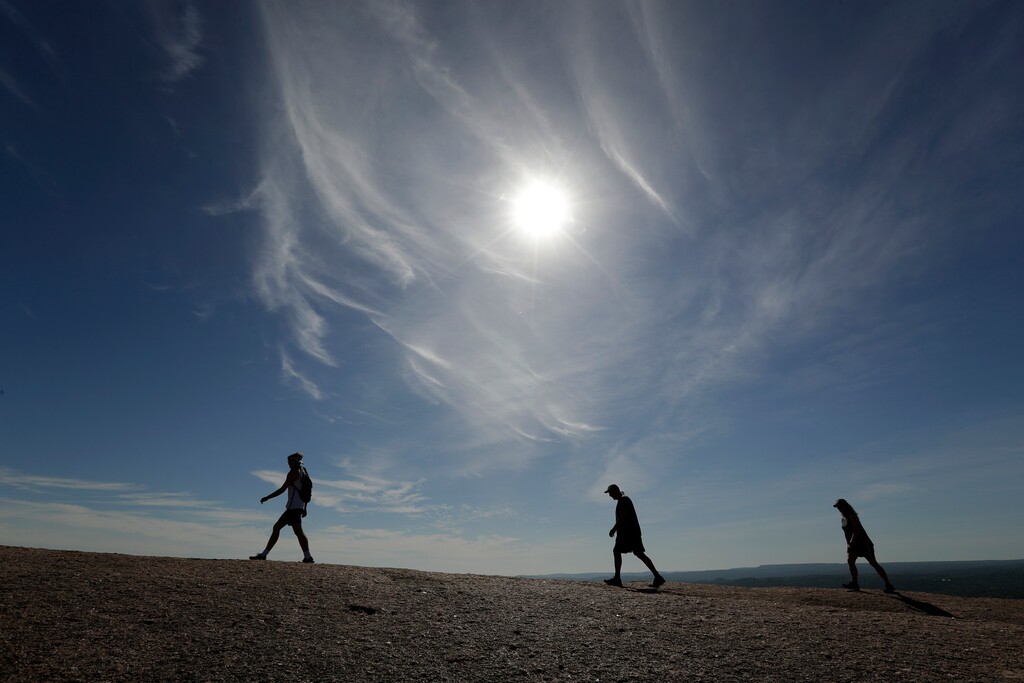 (Eric Gay | AP Photo) Following social distancing rules and wearing face coverings, visitors hike through Enchanted Rock State Park, Monday, April 20, 2020, in Fredericksburg, Texas. Texas state parks are reopened to the public Monday after they had been closed due to the COVID-19 pandemic, but visitors must follow social distancing rules and wear a facial covering or mask.