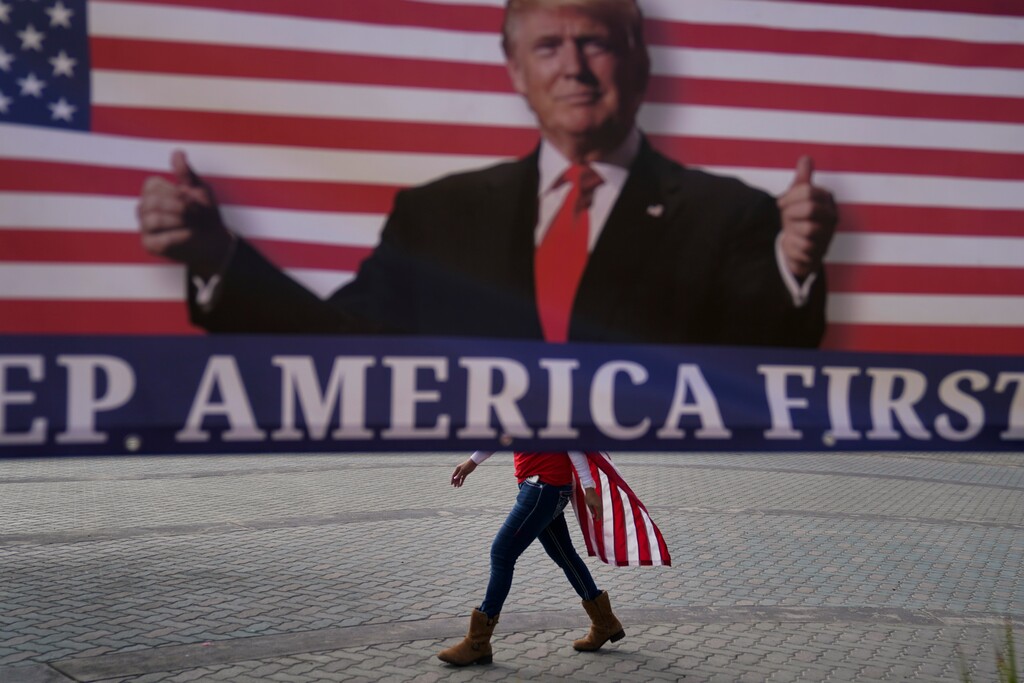 FILE - In this Jan. 6, 2021, file photo, a woman draped in an American flag walks past a banner supporting President Donald Trump during a rally in Huntington Beach, Calif. For America's allies and rivals alike, the chaos unfolding during Donald Trump's final days as president is the logical result of four years of global instability brought on by the man who promised to change the way the world viewed the United States. (AP Photo/Jae C. Hong, File)