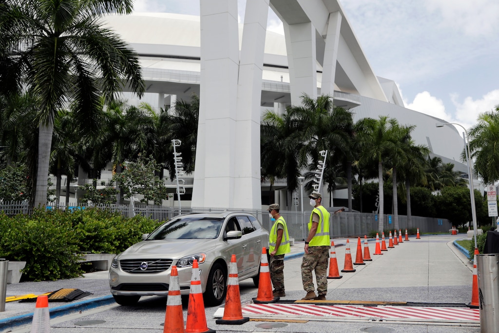 (Lynne Sladky | AP) Members of the Florida National Guard monitor vehicles at a COVID-19 testing site outside of Marlins Park, Monday, July 27, 2020, in Miami. The Marlins home opener against the Baltimore Orioles on Monday night has been postponed as the Marlins deal with a coronavirus outbreak that stranded them in Philadelphia.