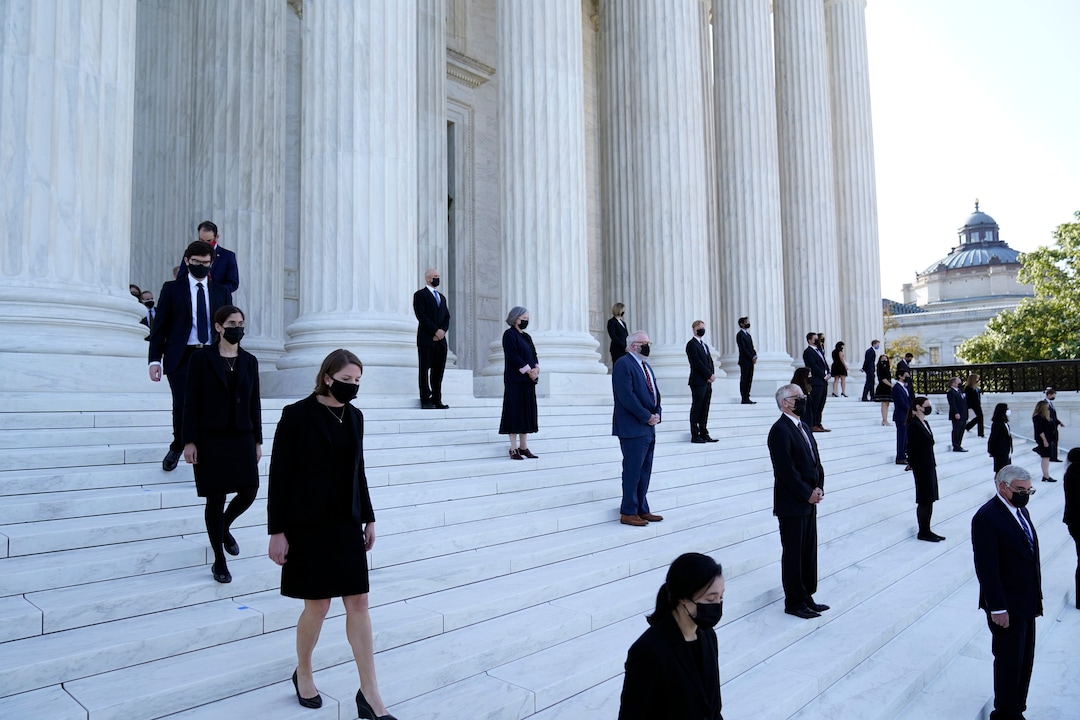 Former law clerks for Justice Ruth Bader Ginsburg stand on the steps of the Supreme Court as they await the arrival of the casket of Ginsburg to arrive at the Supreme Court in Washington, Wednesday, Sept. 23, 2020. Ginsburg, 87, died of cancer on Sept. 18. (AP Photo/Alex Brandon, Pool)