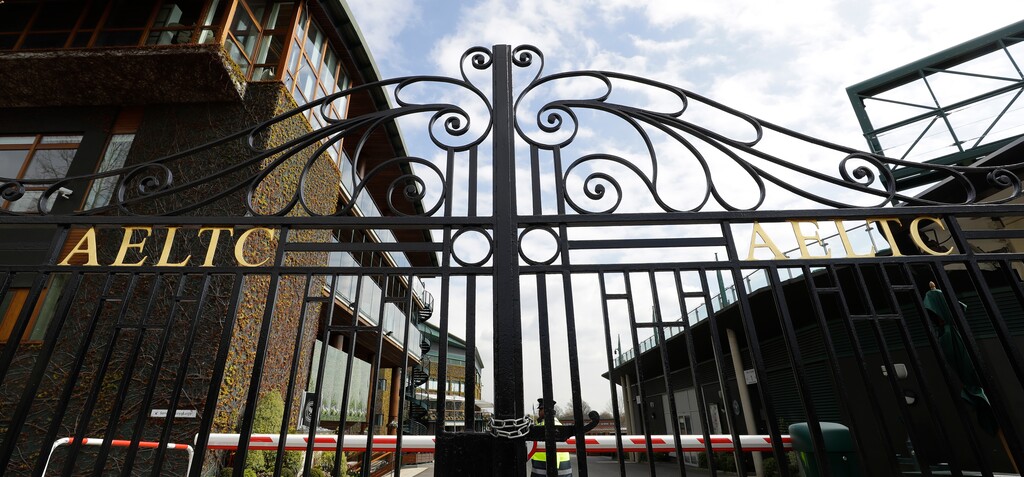 (Kirsty Wigglesworth | AP) A security guard inside the main gates to Wimbledon as it is announced the Wimbledon tennis Championships for 2020 has been canceled due to the coronavirus in London, Wednesday, April 1, 2020. The new coronavirus causes mild or moderate symptoms for most people, but for some, especially older adults and people with existing health problems, it can cause more severe illness or death.