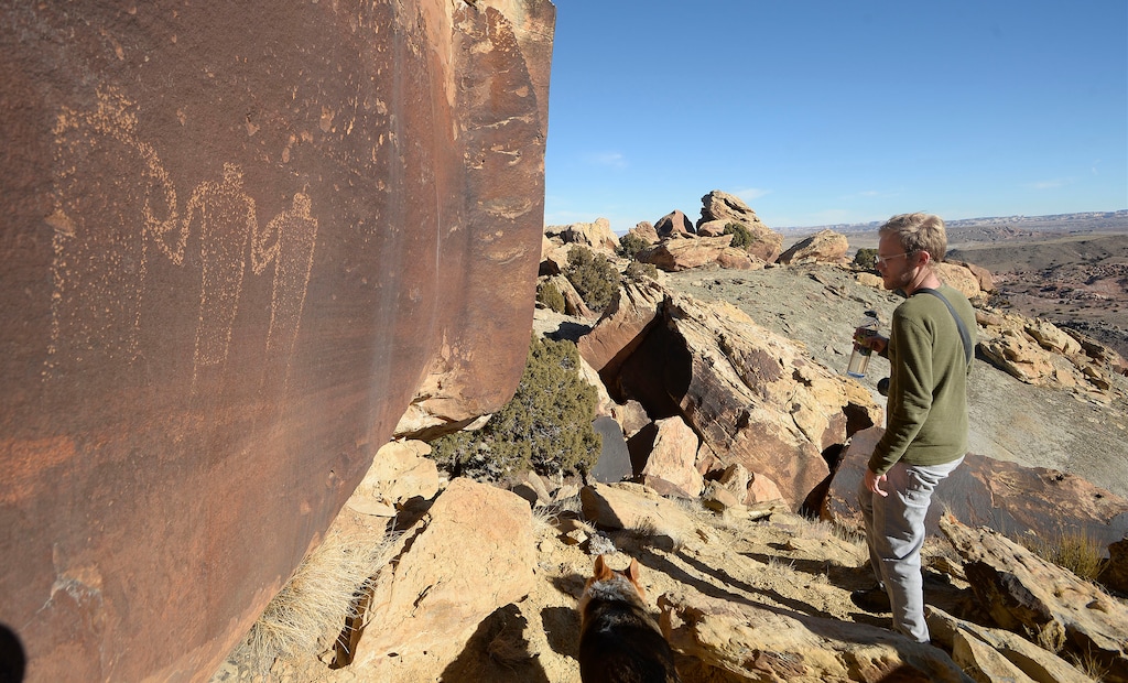 (Al Hartmann  |  Tribune file photo) Photographer Jonathan Bailey passes by Fremont petroglyphs of three figures high in the sandstone caprock in the Molen Reef area of Utah’s San Rafael Swell.  The Bureau of Land Management intends to offer a series of oil and gas leases on public lands in the region, which some say could threaten parts of Molen Reef.  A new study, meanwhile, concludes that leaving oil, gas and coal resources on U.S. public lands undeveloped could have a substantial effect on reducing gas emissions that contribute to climate change.