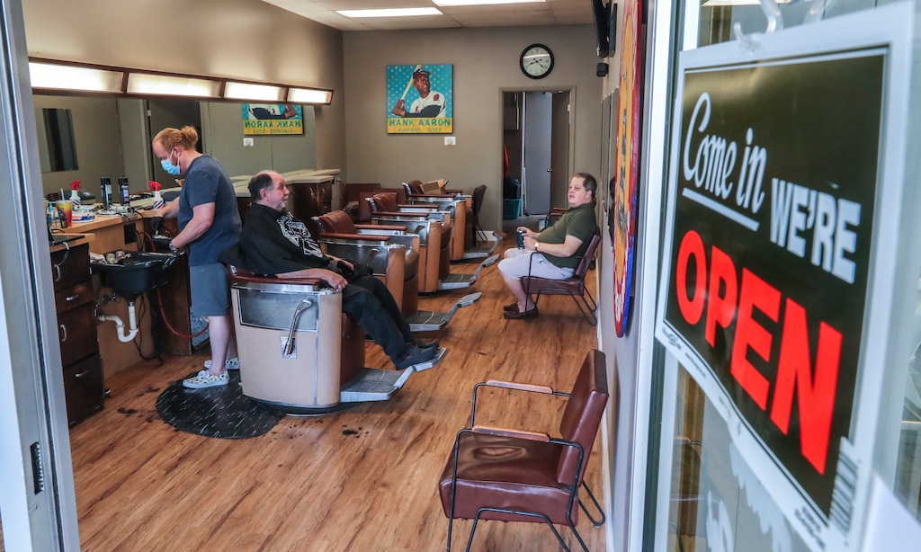 Barber and owner of Chris Edwards, left, wears a mask and cuts the hair of customer at Peachtree Battle Barber Shop in Atlanta on Friday, April 24, 2020. The first phase of Georgia Gov. Brian Kemp's plan to reopen Georgia during the coronavirus pandemic included haircut shops and gyms, though not all chose to open their doors. (John Spink/Atlanta Journal-Constitution via AP)