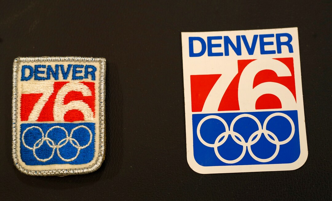 In this Feb. 1, 2018, photo, a patch and sticker used in Colorado's effort to secure an Olympic bid in 1976 are part of the memorabilia collection of the Denver Public Library in Denver. Over 40 years after becoming the first city to walk away from an Olympic bid, Denver is considering whether to try to again to host the Winter Games. (AP Photo/David Zalubowski)