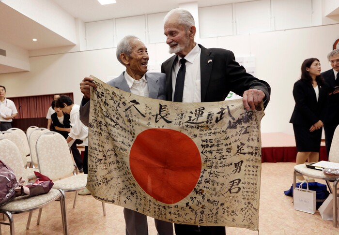 WWII veteran Marvin Strombo, right, and Tatsuya Yasue, 89-year-old farmer, hold a Japanese flag with autographed messages which was owned by his brother Sadao Yasue, who was killed in the Pacific during World Work II, during a ceremony in Higashishirakawa, in central Japan's Gifu prefecture Tuesday, Aug. 15, 2017. Strombo has returned to the fallen soldier's family the calligraphy-covered flag he took from the man's body 73 years ago. (AP Photo/Eugene Hoshiko)