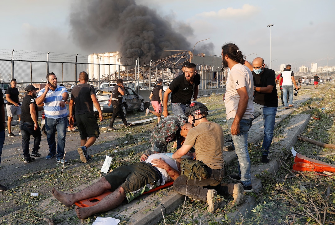 EDS NOTE: GRAPHIC CONTENT - Rescue workers help an injured man at the explosion scene that hit the seaport of Beirut, Lebanon, Tuesday, Aug. 4, 2020. Massive explosions rocked downtown Beirut on Tuesday, flattening much of the port, damaging buildings and blowing out windows and doors as a giant mushroom cloud rose above the capital. Witnesses saw many people injured by flying glass and debris. (AP Photo/Hussein Malla)