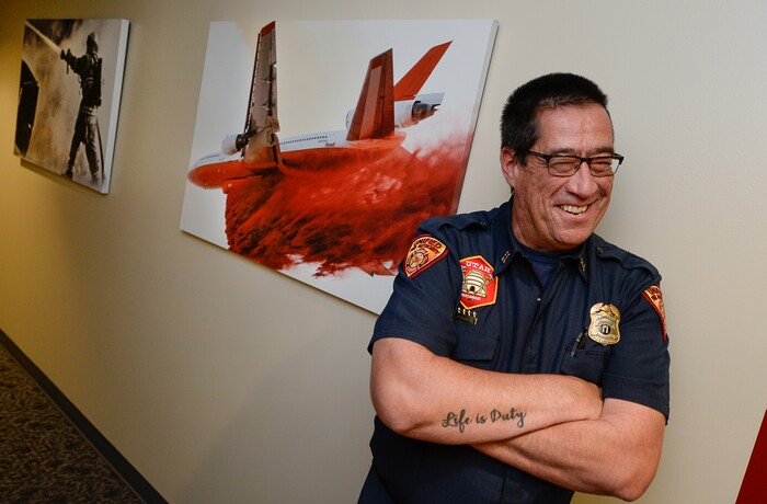 (Francisco Kjolseth  |  The Salt Lake Tribune)  Fitzgerald Petersen, a captain with Unified Fire Authority is teased by a passing colleague as he poses for a photograph alongside some of his work on display at UFA headquarters. Petersen often has a front row seat to documenting his colleagues on the fire line. For the past 17 years he's been the department's firefighter. In that capacity, he listens to his radio on his off days and responds to incidents to document his coworkers.