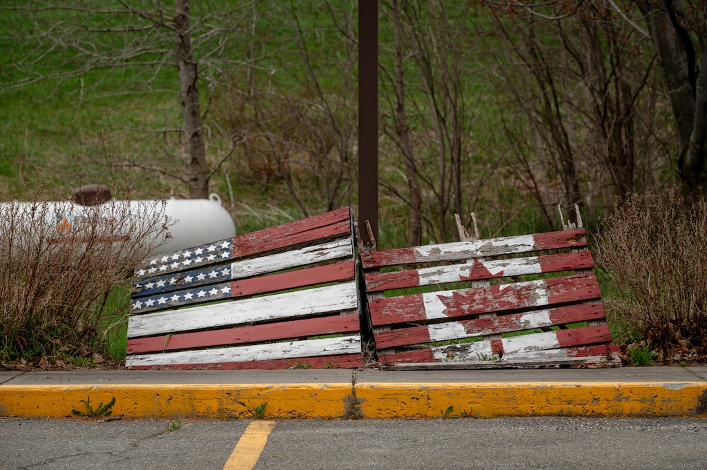 (Hilary Swift | The New York Times) Wooden versions of the American flag and Canadian flag decorate a sidewalk in Derby Line, Vt., April 30, 2025.