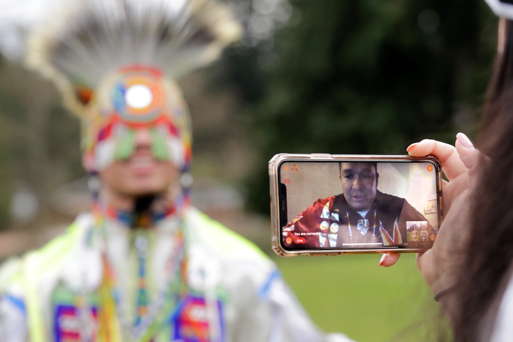 (Elaine Thompson | AP) In this photo taken Saturday, April 4, 2020, moderator Whitney Rencountre, a Crow Creek Dakota tribal member, is seen on a screen from Rapid City, S.D., as he talks with Wakiyan Cuny, a Dakota and Lakota tribal member, during a live streamed powwow, in Puyallup, Wash. The largest powwows in the country have been canceled or postponed amid the spread of the coronavirus. Tribal members have found a new outlet online with the Social Distance Powwow. They're sharing videos of colorful displays of culture and tradition that are at their essence meant to uplift people during difficult times.
