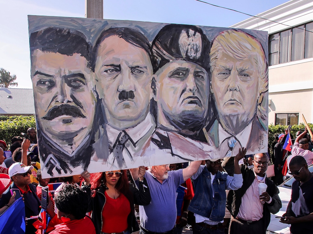 Haitian community members hold an image depicting image shows from left, Joseph Stalin, Adolf Hitler, Benito Mussolini and President Donald Trump during a protest near Trump's Mar-a-Lago estate Monday, Jan. 15, 2018, in West Palm Beach, Fla. (Damon Higgins/Palm Beach Post via AP)