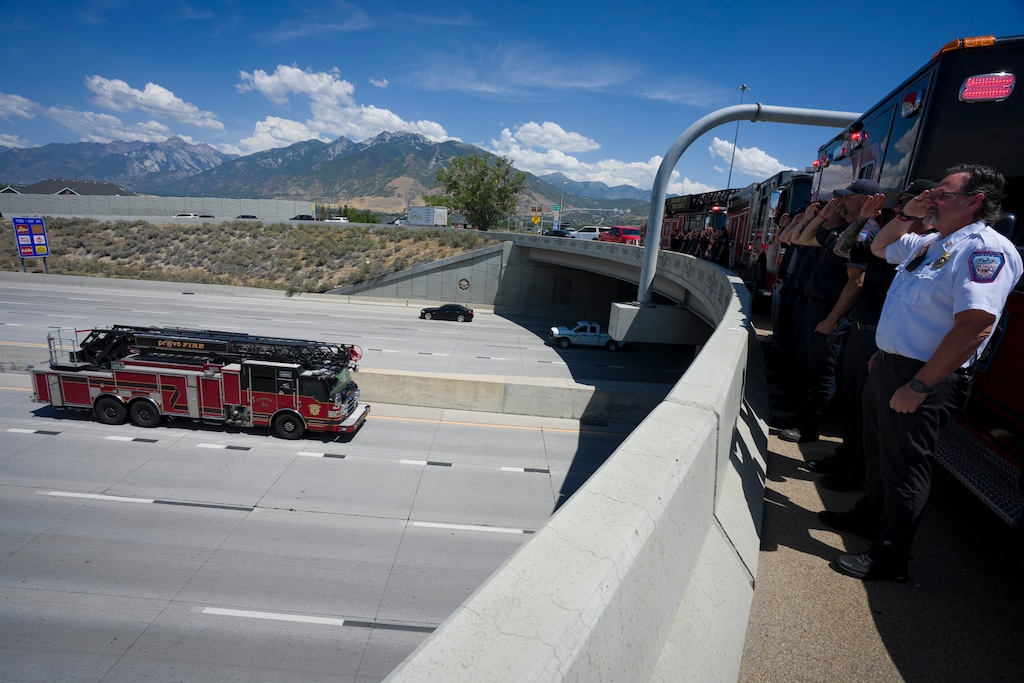(Bethany Baker | The Salt Lake Tribune) Draper firefighters stand at attention on the Bangerter Highway overpass along Interstate 15 in Draper on Tuesday, July 21, 2026 as a Provo fire truck leads the procession transporting the bodies of Provo Fire Capt. Spencer Long, his wife, Katrina, and their three sons, who all died in a flash flood near a Wayne County campground on Friday, to a funeral home in Spanish Fork.