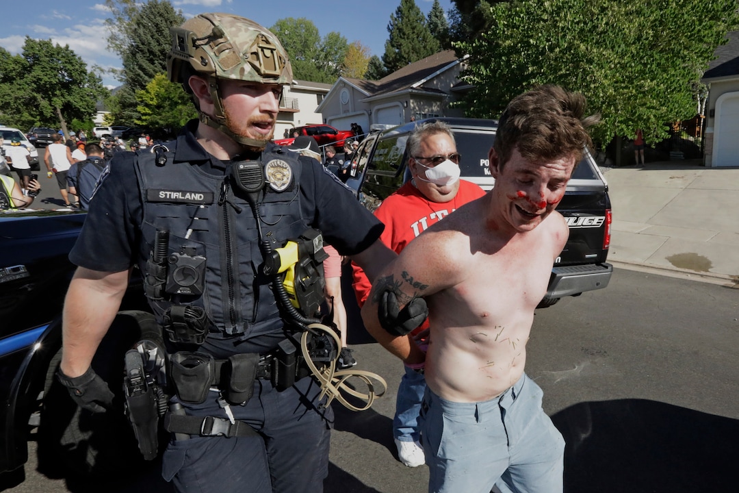 A protester is led away after being taken into custody by Cottonwood Heights police officers during a march Sunday, Aug. 2, 2020, in Cottonwood Heights, Utah. The protest was a "March for Justice" focused largely around Zane James, who was fatally shot by police in Cottonwood Heights in 2018. (AP Photo/Rick Bowmer)