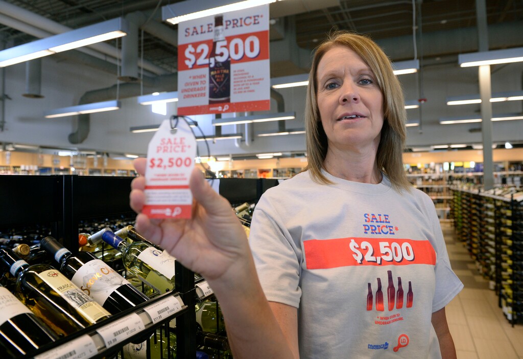 (Al Hartmann | Tribune file photo) Val Dunaway, regional manager for 22 Utah State Liquor Stores, shows employee shirts, posters and tags hanging from liquor bottles reminding patrons of the legal and financial costs of supplying alcohol to those who are underage, part of a MADD, DABC and Parents Empowered program.