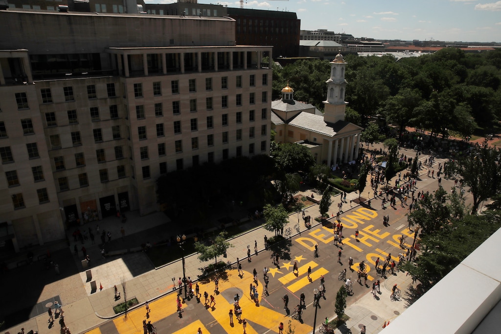 (Maya Alleruzzo | The Associated Press) People walk on the words "defund the police" that was painted in bright yellow letters on 16th Street as demonstrators protest Sunday, June 7, 2020, near the White House in Washington, over the death of George Floyd, a black man who was in police custody in Minneapolis. Floyd died after being restrained by Minneapolis police officers on Memorial Day.