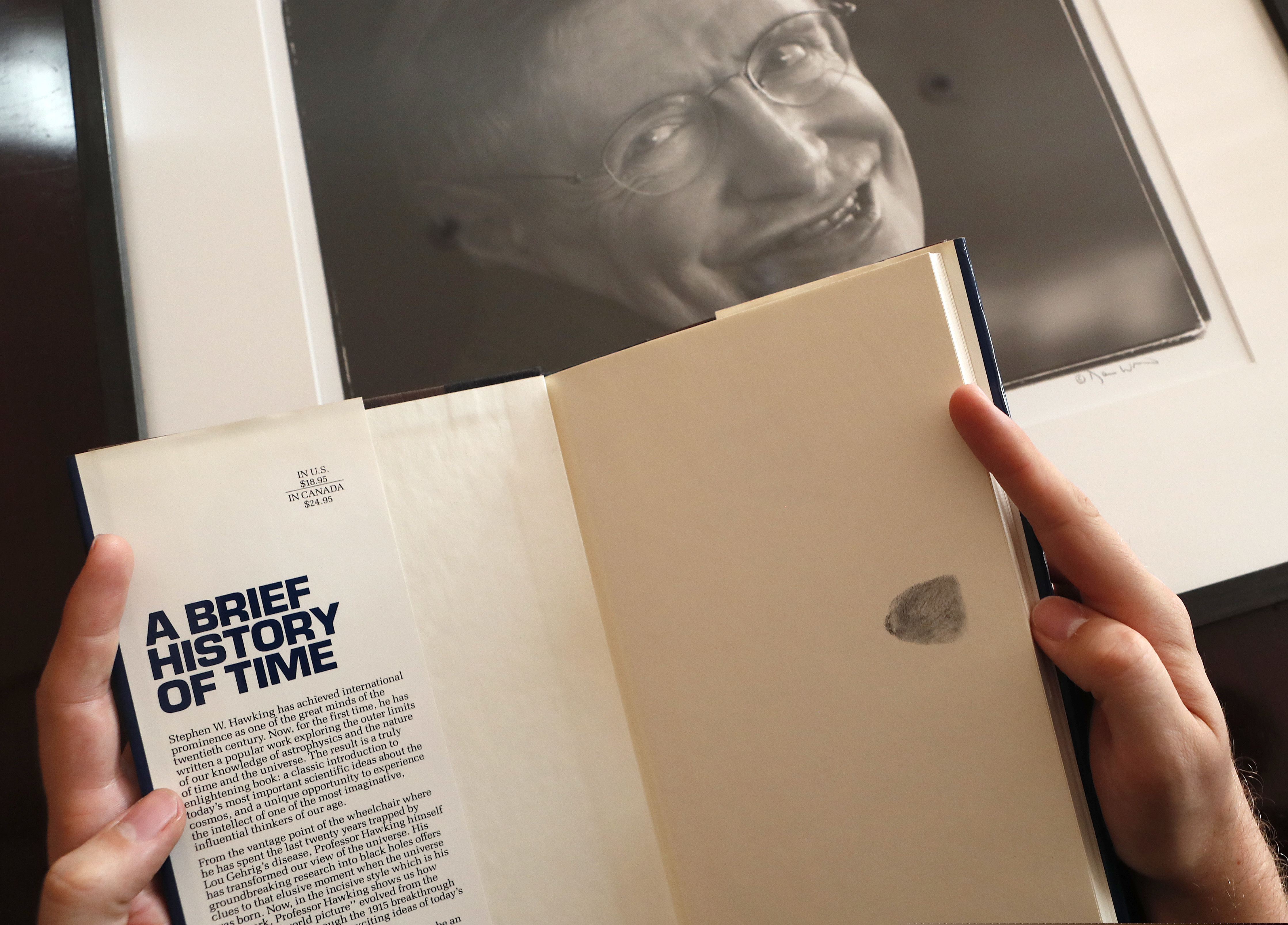 A Book, signed with a thumb print by Stephen Hawking is one of the personal and academic possessions of Stephen Hawking, photo behind, at the auction house Christies in London, Friday, Oct. 19, 2018. The online auction announced Monday Oct. 22, 2018, by auctioneer Christie’s features 22 items from Hawking, including his doctoral thesis on the origins of the universe, with the sale scheduled for 31 October and 8 November. (AP Photo/Frank Augstein)