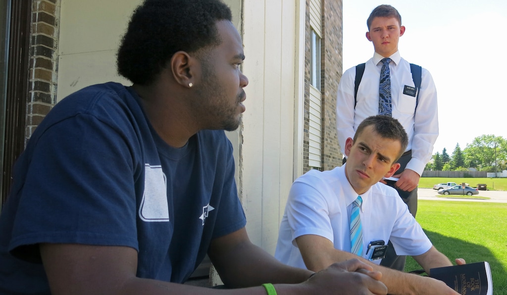 (John Enger | Minnesota Public Radio) In this June 13, 2018 photo, Mormon missionaries Tanner Smedley, seated, and Joseph Smith talk with a man identified only as Devontae in Detroit Lake, Minn. Smedley and Smith both 19 from Utah, are part way through into their two-year Mormon mission. They have spent most of that mission assigned to Detroit Lakes.