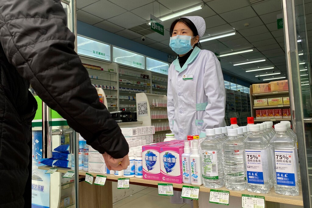 (Ng Han Guan | AP) A pharmacy worker attends to visitors at the store entrance in Beijing, China on Thursday, Feb. 20, 2020.