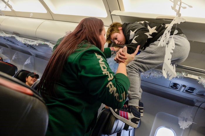 (Leah Hogsten | The Salt Lake Tribune) Tiffany Burgess of Seattle coaxes her son Zander, 11, out of the overhead bins as the Salt Lake City Gold Star families board the flight. Ten Gold Star families from Salt Lake City were treated to a Winter Wonderland scene, including Whoville and the Grinch at their boarding gate at Salt Lake International Airport, Dec. 7, 2019 before their flight to Disney World aboard the Snowball Express. This month, the Gary Sinise Foundation's Snowball Express will fly more than 1,700 family members of fallen U.S. military heroes to Disney World for a holiday retreat.