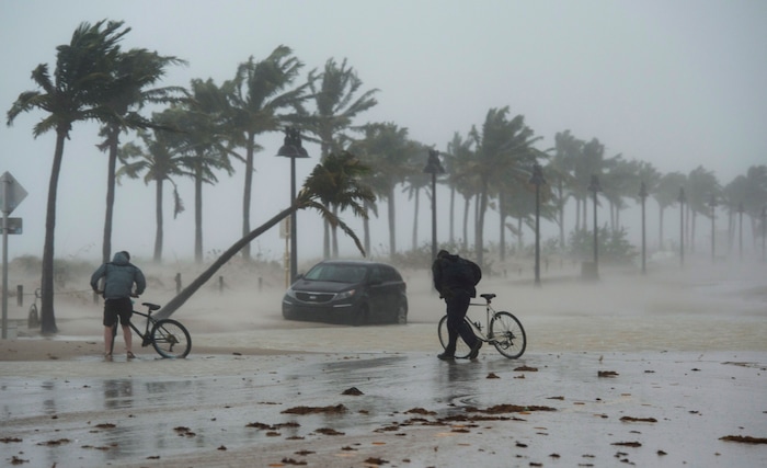 (Paul Chiasson/The Canadian Press via AP) Two men walk their bicycle along a flooded street on the waterfront of Fort Lauderdale, Fla., as Hurricane Irma passes through on Sunday, Sept. 10, 2017.